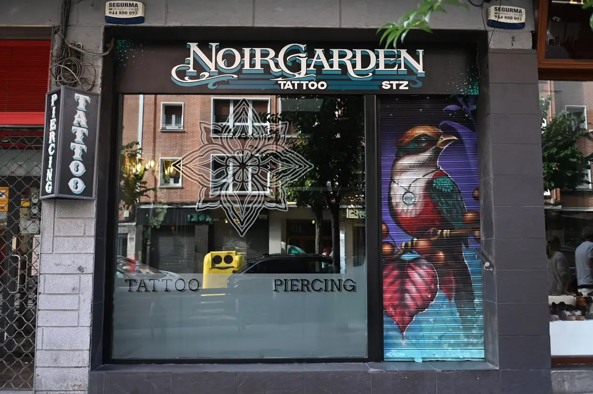 Fachada de Noir Garden Tattoo en Santurtzi, con el escaparate de tattoo y piercing y la persiana pintada con un pájaro